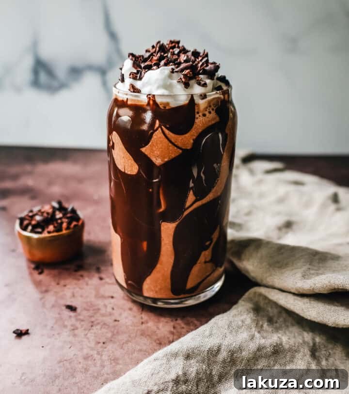 Delicious Chocolate Almond Butter Smoothie in a glass, topped with whipped cream and cacao nibs.