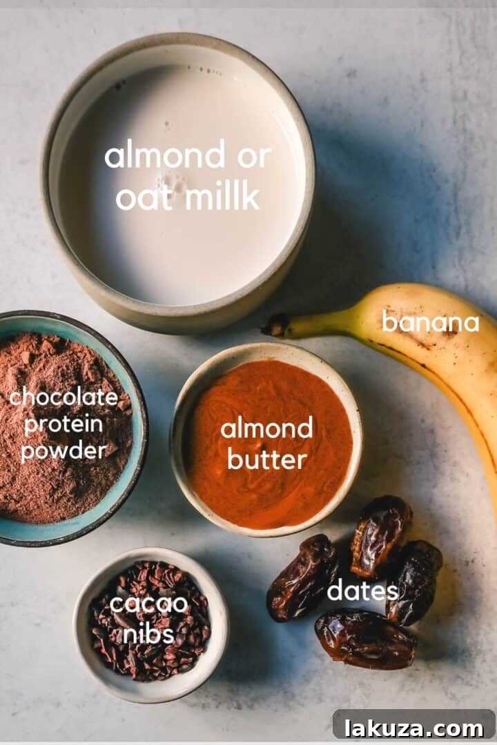 Ingredients for a healthy Chocolate Protein Shake, including chocolate powder, almond milk, almond butter, dates, and a frozen banana.