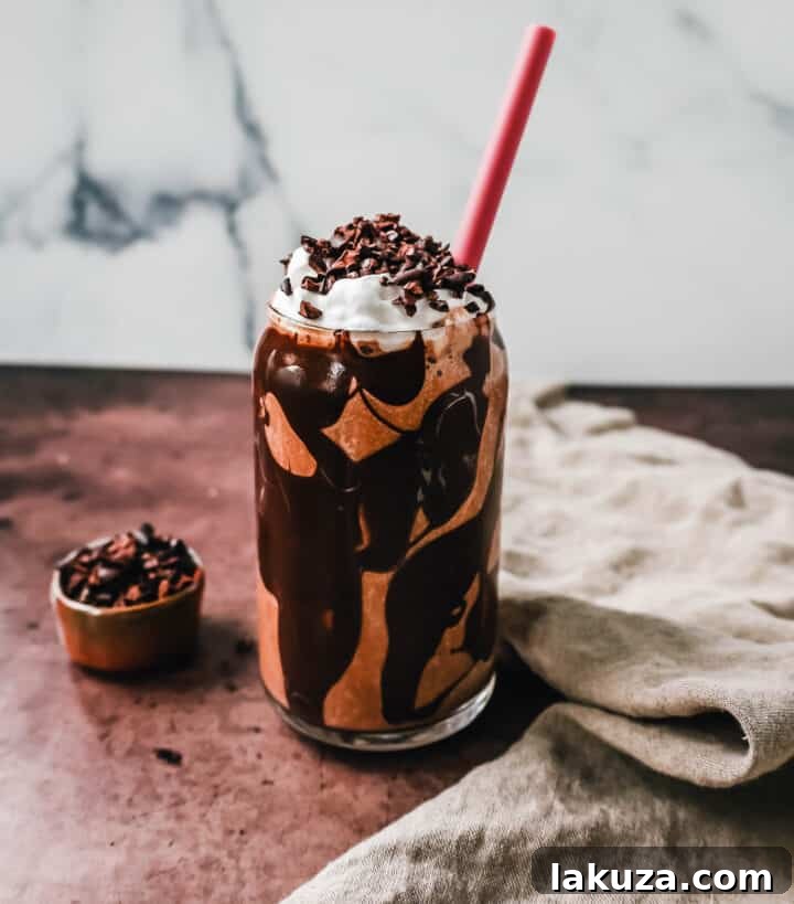 A rich Chocolate Almond Butter Smoothie being poured into a glass drizzled with melted dark chocolate.