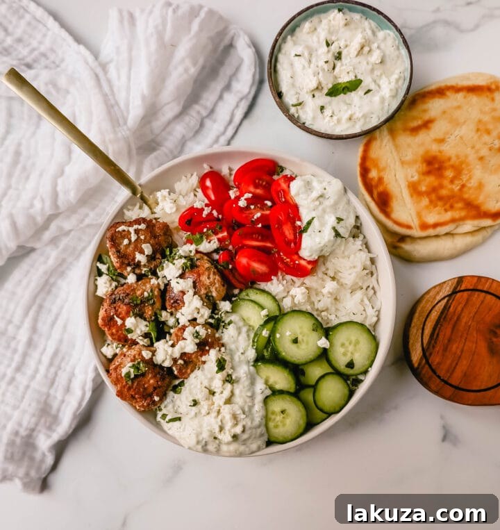 A close-up of a Greek Chicken Meatball Bowl with tzatziki, fresh vegetables, and rice.