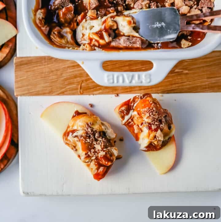 A tempting image of a Caramel Apple Toffee Dip in a clear dish, featuring a smooth, light brown cream cheese base, topped with a glossy caramel layer and abundant toffee crumbles. Freshly sliced apples are arranged enticingly around the dip.