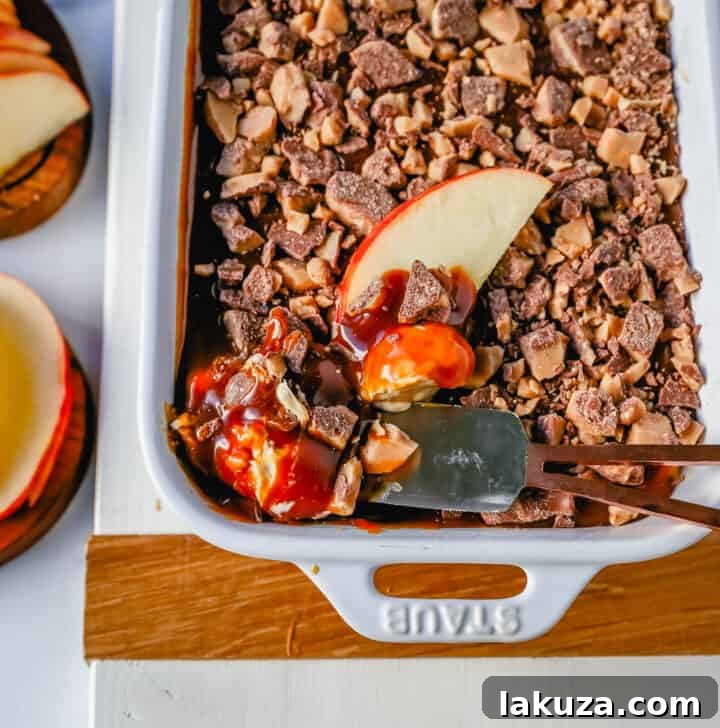 A close-up view of the irresistible Caramel Apple Toffee Dip, highlighting its smooth, creamy texture, rich caramel swirl, and crunchy toffee bits. A single apple slice is poised, ready to scoop up the delicious dessert.