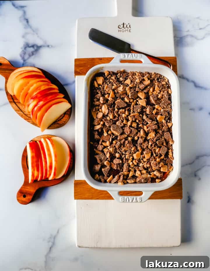 A top-down view of the Caramel Apple Toffee Dip served in a square dish, featuring a rich layer of caramel and crunchy toffee bits. It's surrounded by an abundance of crisp green and red apple slices, inviting guests to dip and enjoy.