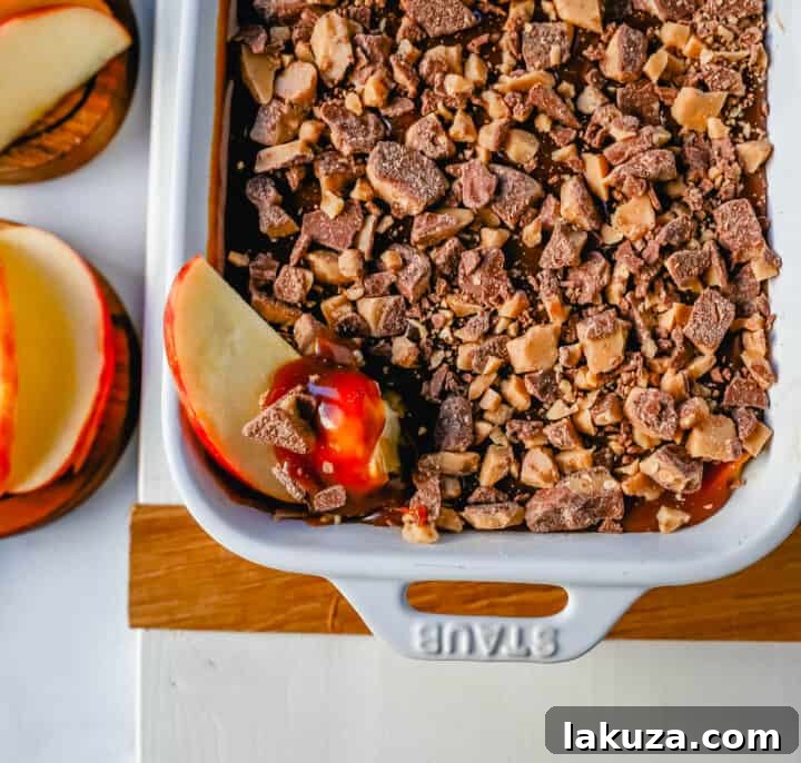 A vibrant, inviting image of the Caramel Apple Toffee Dip, ready for a party. The creamy dip is artfully swirled with caramel and dotted with toffee pieces, surrounded by a generous spread of freshly sliced red apples on a rustic wooden board.