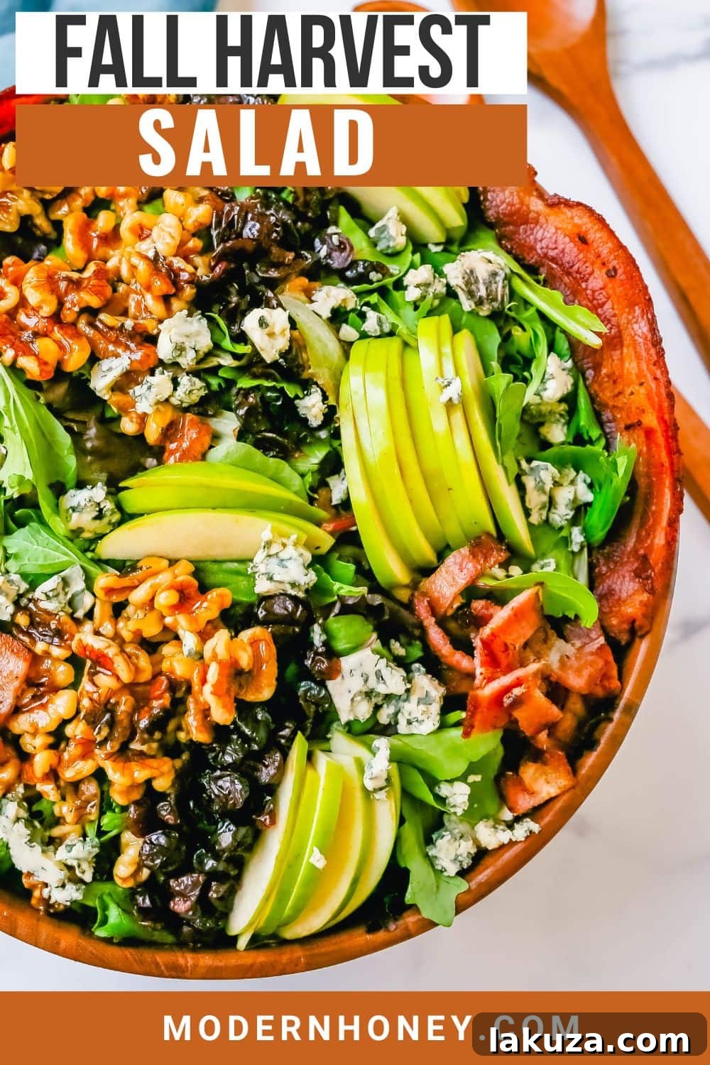 A large serving of Fall Harvest Salad artfully arranged in a bowl, showing the texture and color variety of apples, candied walnuts, dried cranberries, cheese, bacon, and mixed greens.