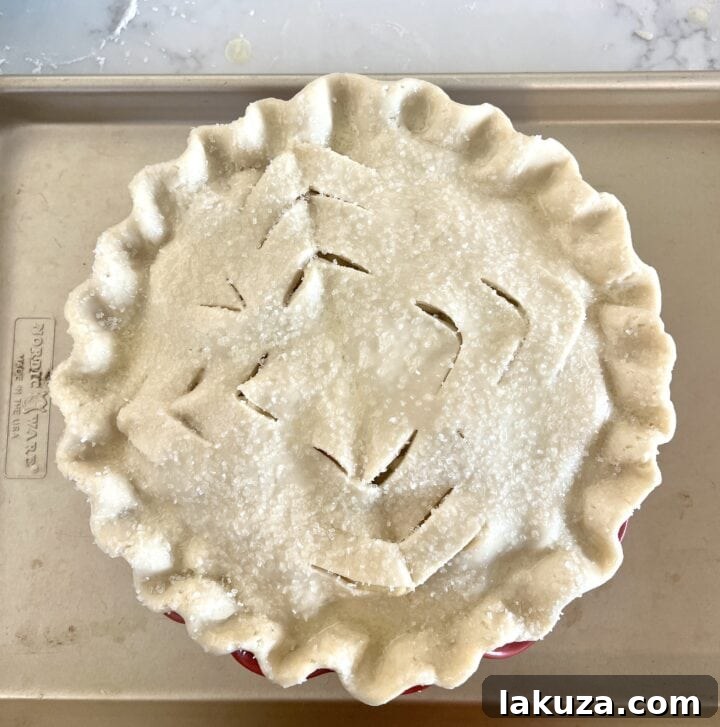 Unbaked apple pie with a decorative crimped crust and sugar sprinkled on top, ready for the oven.