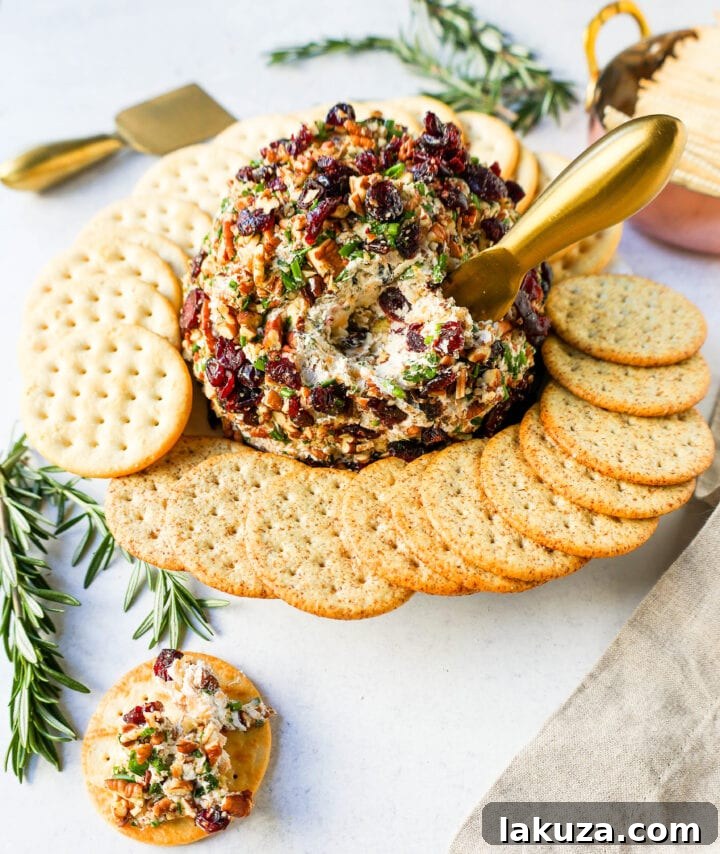 A festive Cranberry Pecan Cheese Ball, generously coated with chopped pecans and dried cranberries, presented on a wooden board.