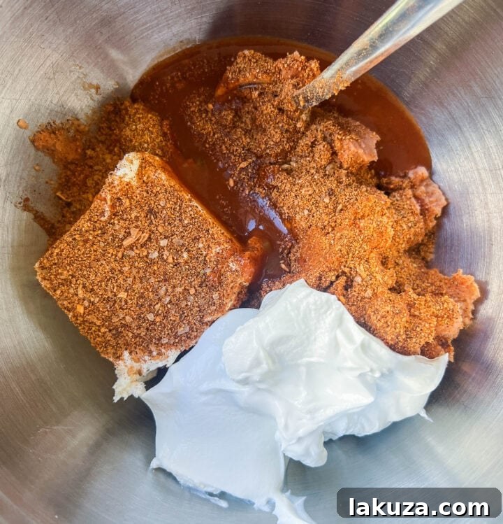 Various ingredients for a hot bean and cheese dip laid out on a counter, including canned refried beans, sour cream, cream cheese, taco seasoning, hot sauce, and shredded Mexican cheese.