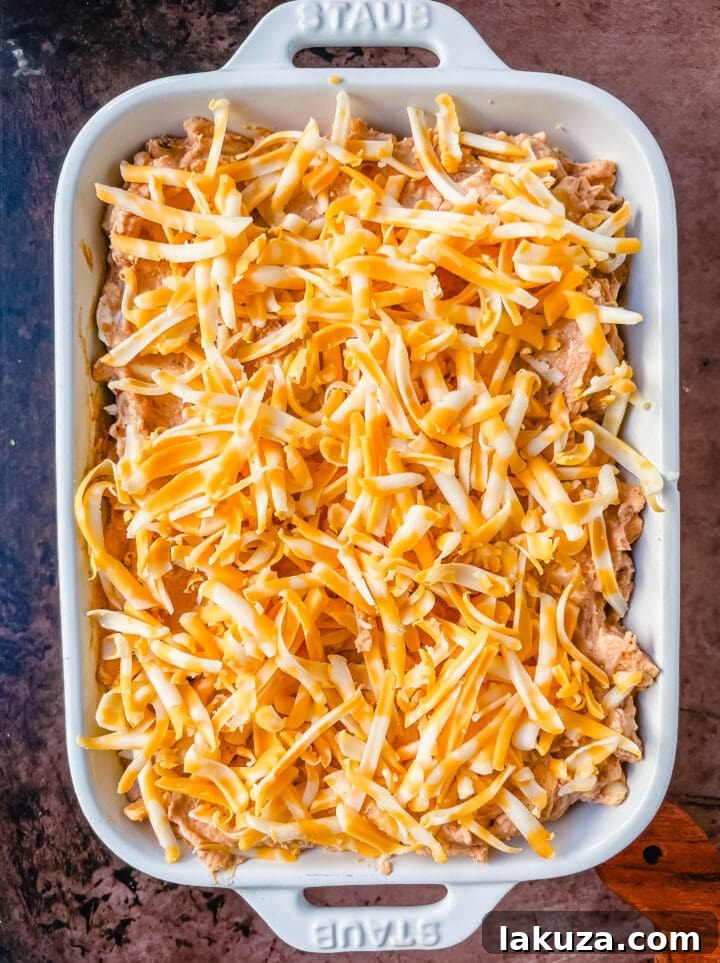 A bowl of uncooked bean dip mixture, showing the creamy texture and integrated ingredients before baking and topping with extra cheese.