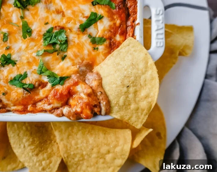 A fully baked hot bean and cheese dip, garnished with fresh cilantro and a dollop of sour cream, ready to be scooped with tortilla chips.
