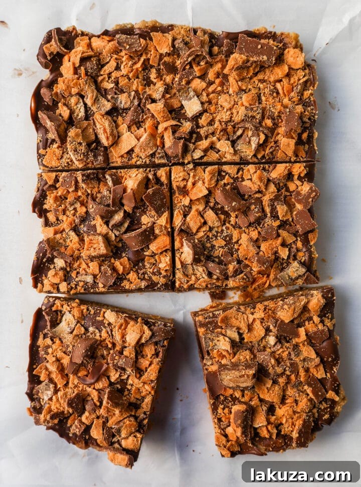 Ultimate Butterfinger Crunch Bars 3 Up-close shot of a freshly made batch of Crunchy Butterfinger Bars, showing the layered texture of graham cracker base, Butterfinger bits, and chocolate topping.