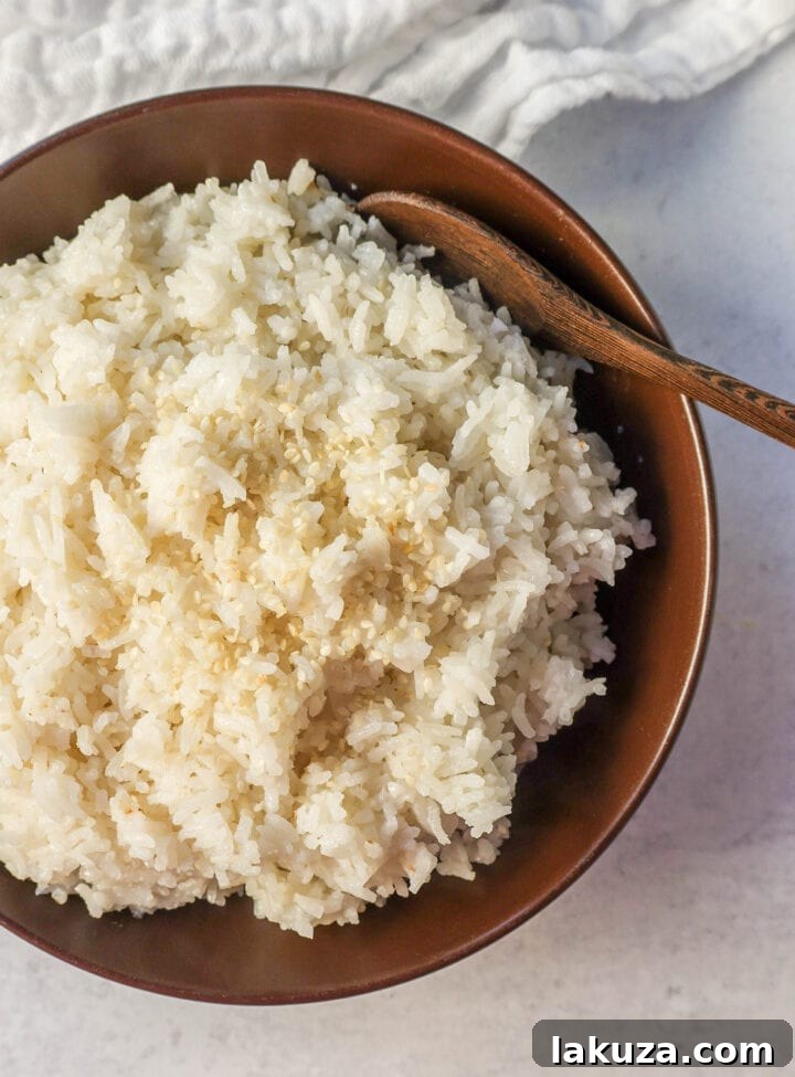 A serving of freshly cooked fluffy Coconut Rice in a bowl, garnished with green herbs, ready to be enjoyed as a savory and slightly sweet side dish.
