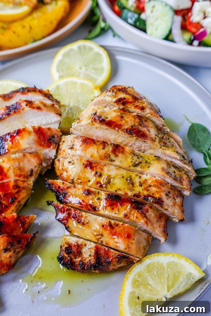 Close-up of marinated raw Greek chicken pieces in a bowl, glistening with olive oil, lemon, garlic, and oregano before grilling.