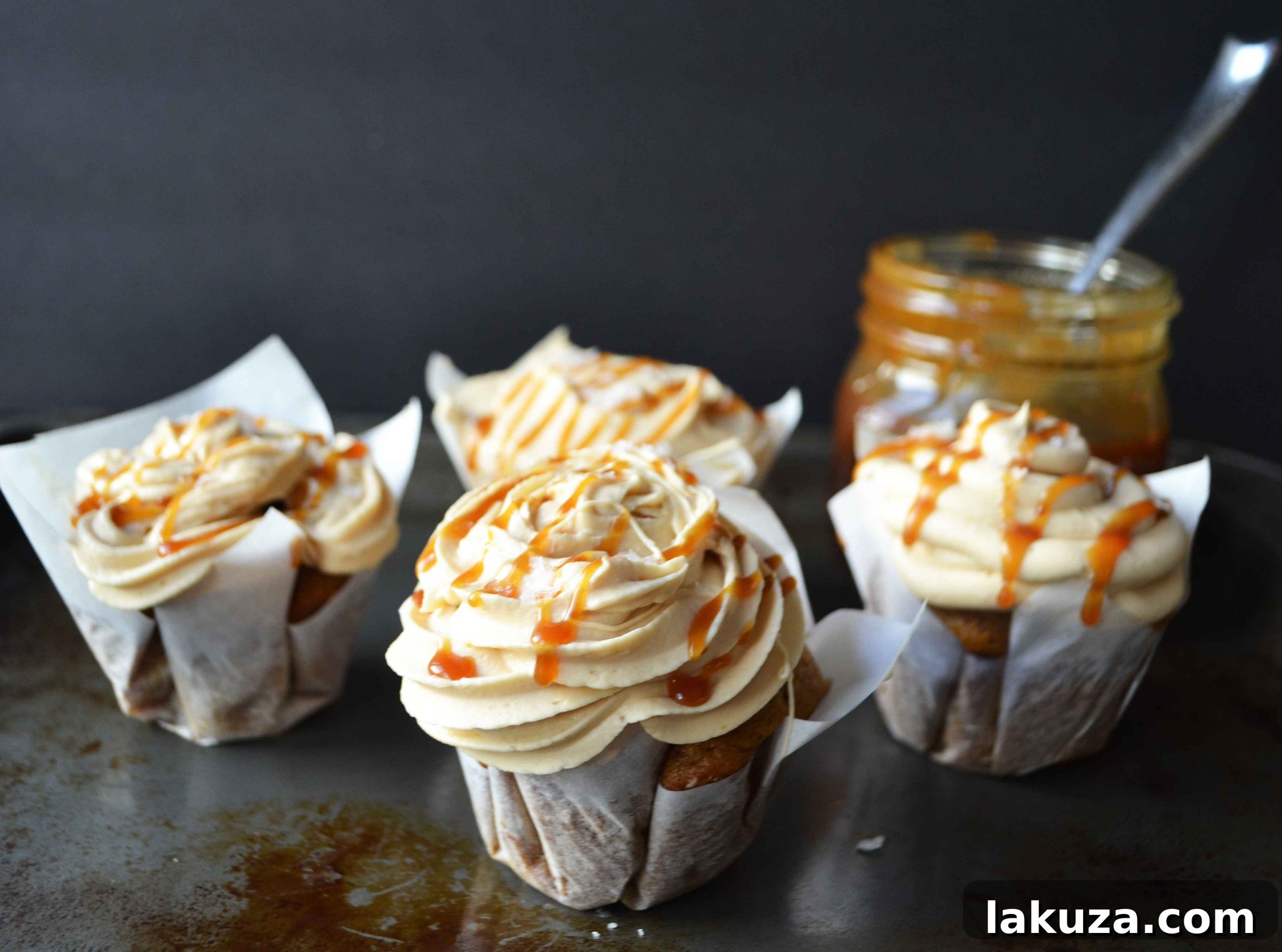Two beautifully presented pumpkin cupcakes, adorned with creamy salted caramel frosting and a rich caramel drizzle, perfect for autumn indulgence.