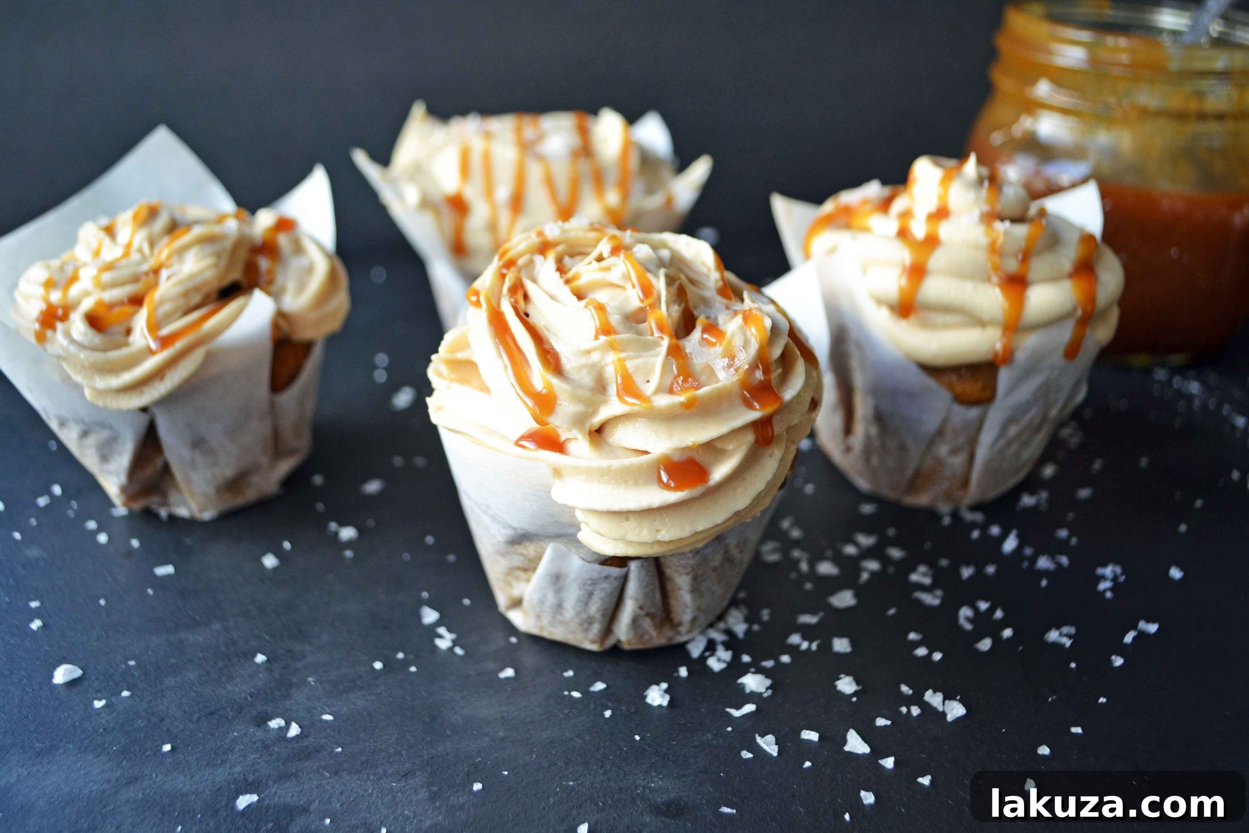 A festive display of several pumpkin cupcakes, each adorned with a generous swirl of salted caramel frosting, ideal for a Fall gathering or dessert table.