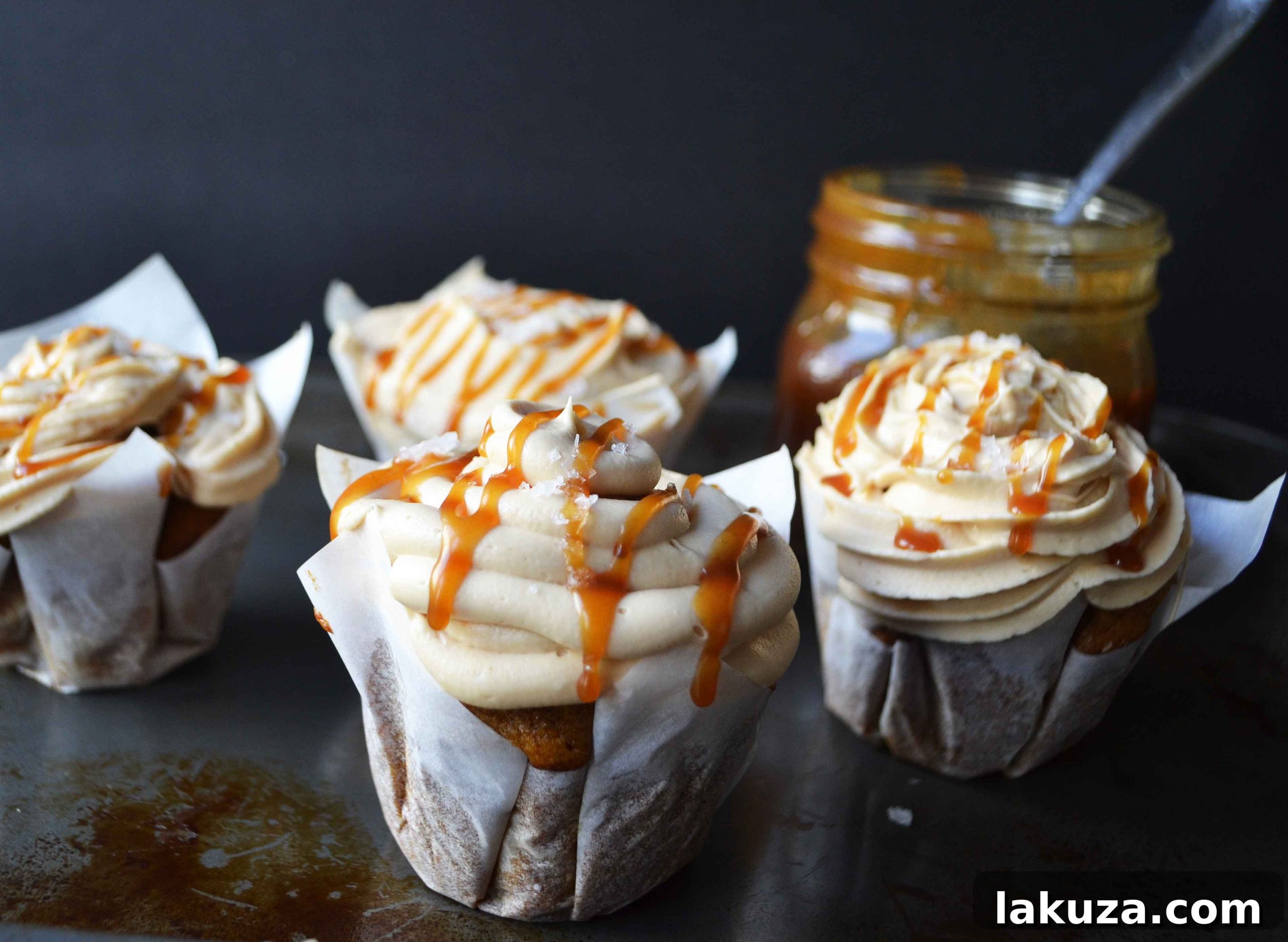 A close-up shot of a beautifully frosted pumpkin cupcake, featuring a perfect swirl of salted caramel frosting, drizzled with extra caramel, and sprinkled with sea salt.