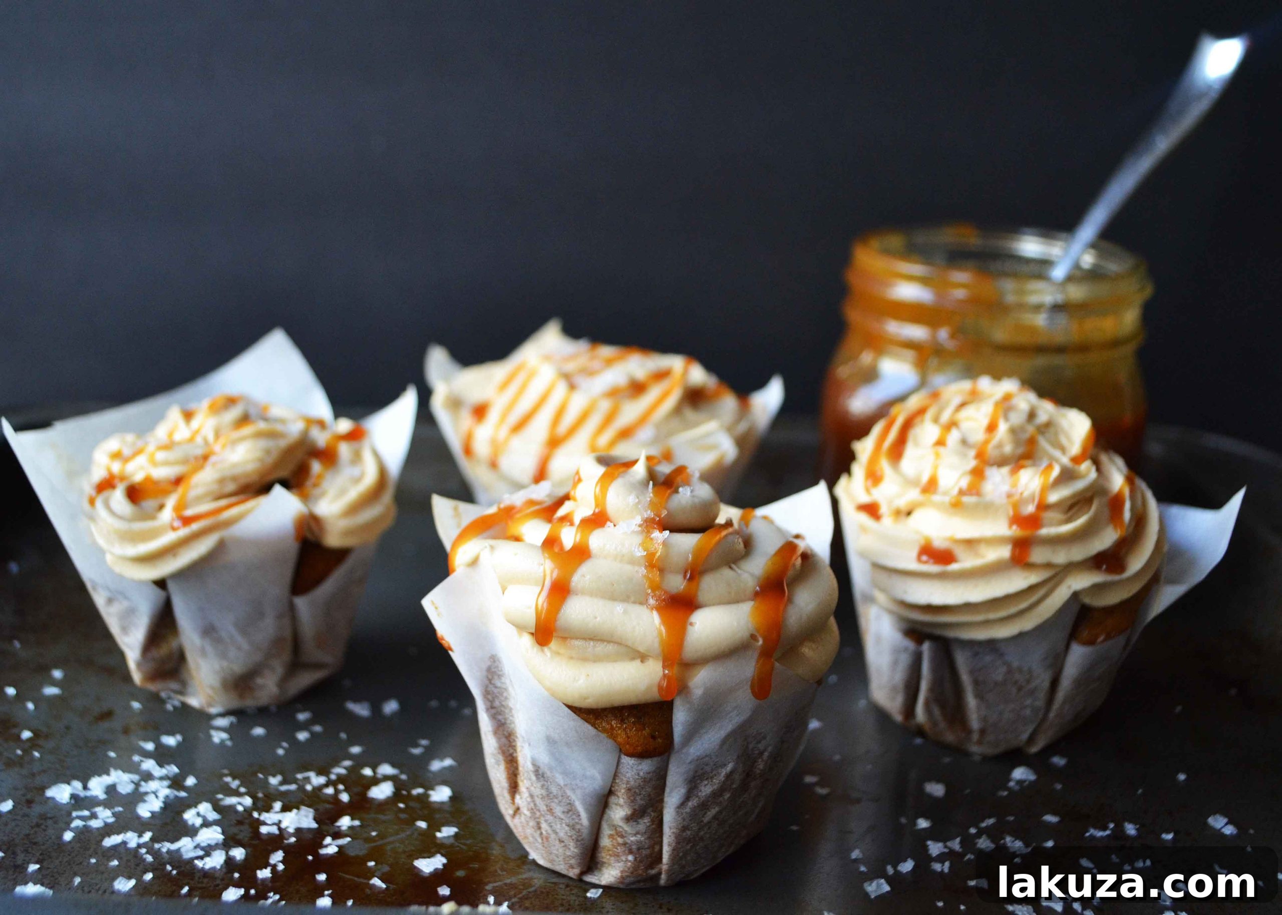 Two perfectly frosted salted caramel pumpkin cupcakes arranged on a rustic wooden board, evoking cozy fall vibes.
