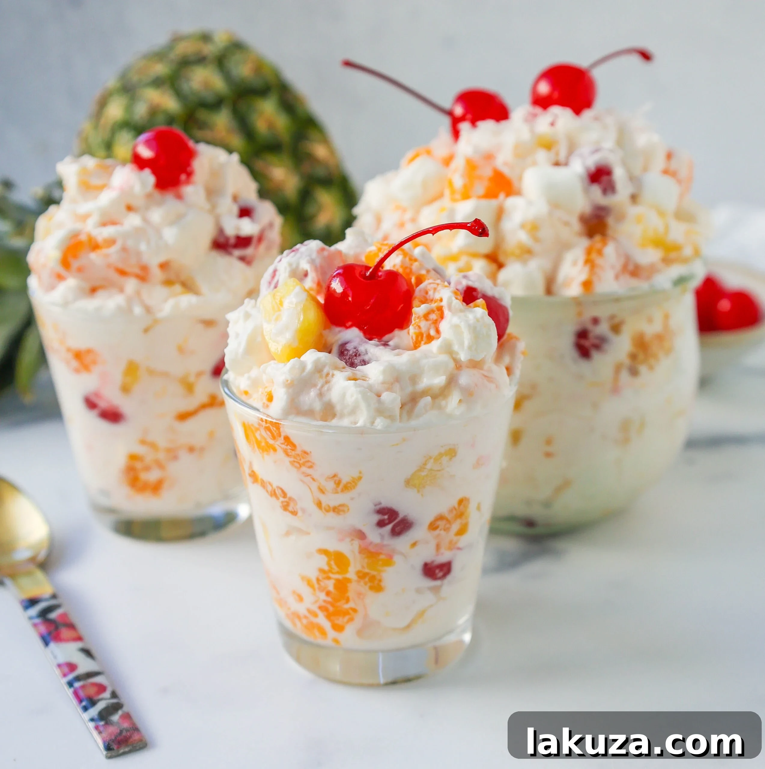 Sweet Ambrosia Cloud 3 Close-up of fluffy Ambrosia Salad in a glass bowl, showcasing fresh pineapple chunks, bright mandarin oranges, ruby red maraschino cherries, white marshmallows, and delicate coconut flakes, all coated in a creamy, sweet dressing.
