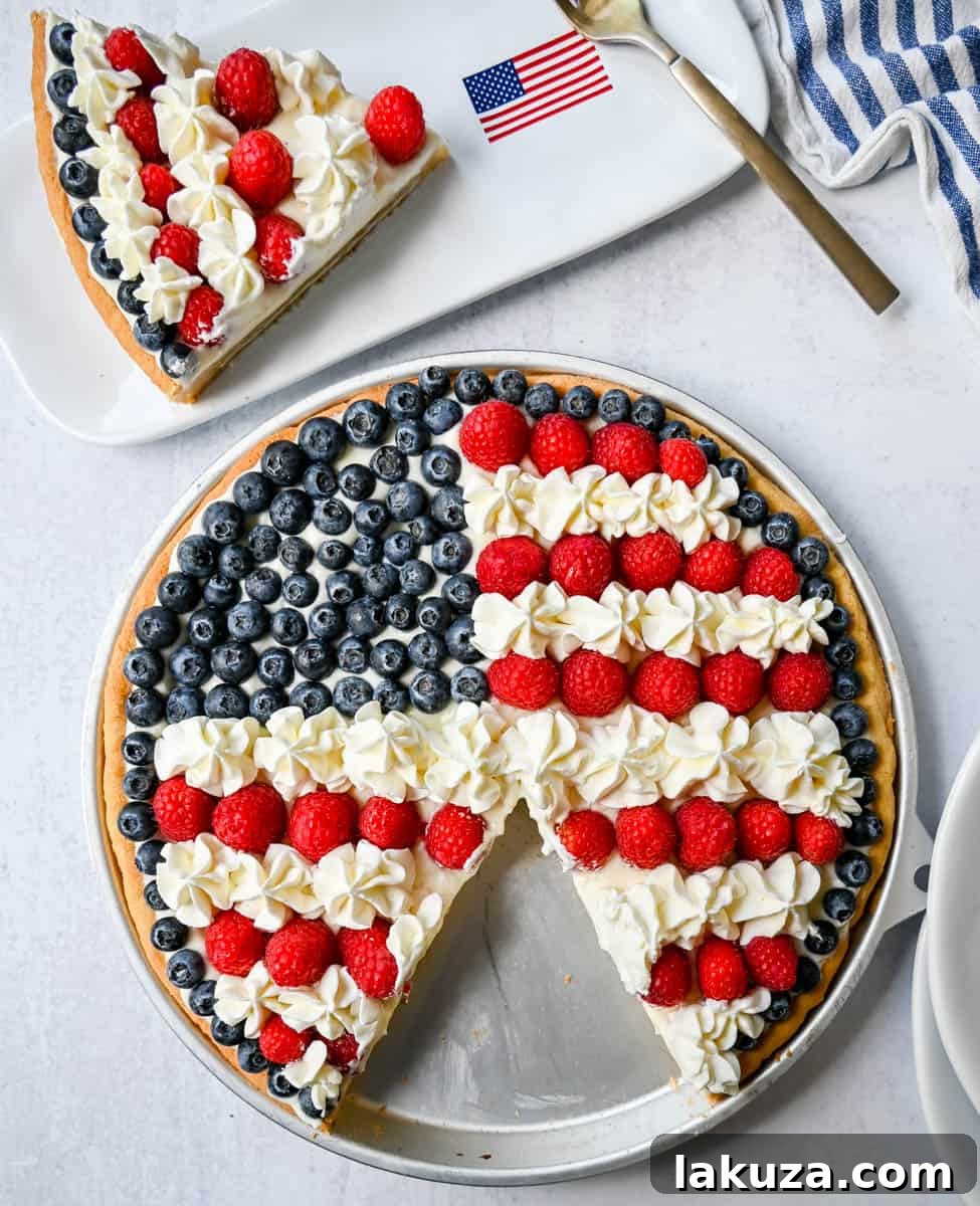 Close-up of the patriotic Sugar Cookie Flag Fruit Pizza, showcasing the vibrant red raspberries forming stripes, blue blueberries for the stars, and white cream cheese frosting on a golden sugar cookie crust.
