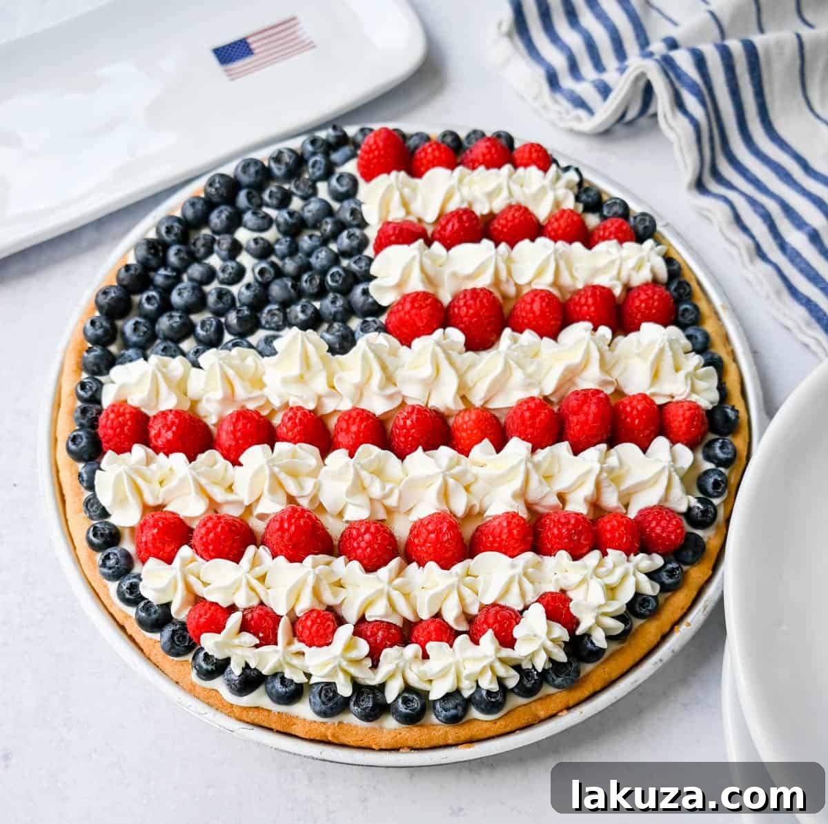 A slice of the Sugar Cookie Flag Fruit Pizza, showing the soft cookie crust, creamy filling, and a perfect arrangement of raspberries, blueberries, and whipped cream.