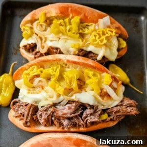 The Best Slow Cooker Italian Beef Sandwiches with provolone, caramelized onions, and pepperoncinis.