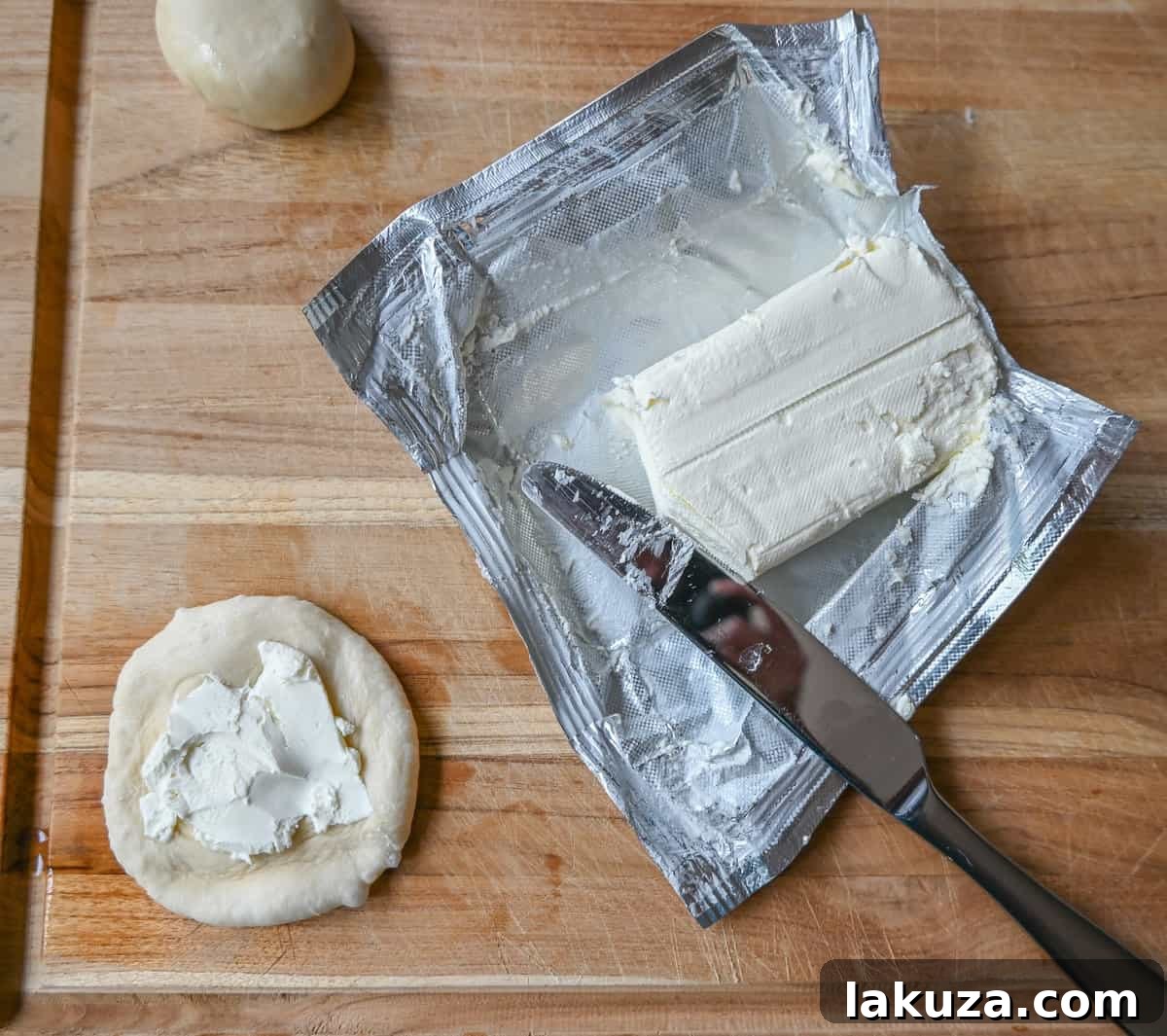 Hands carefully placing a generous scoop of cream cheese onto a flattened dough disc, preparing to create the viral Cream Cheese Filled Everything Bagel Bites.