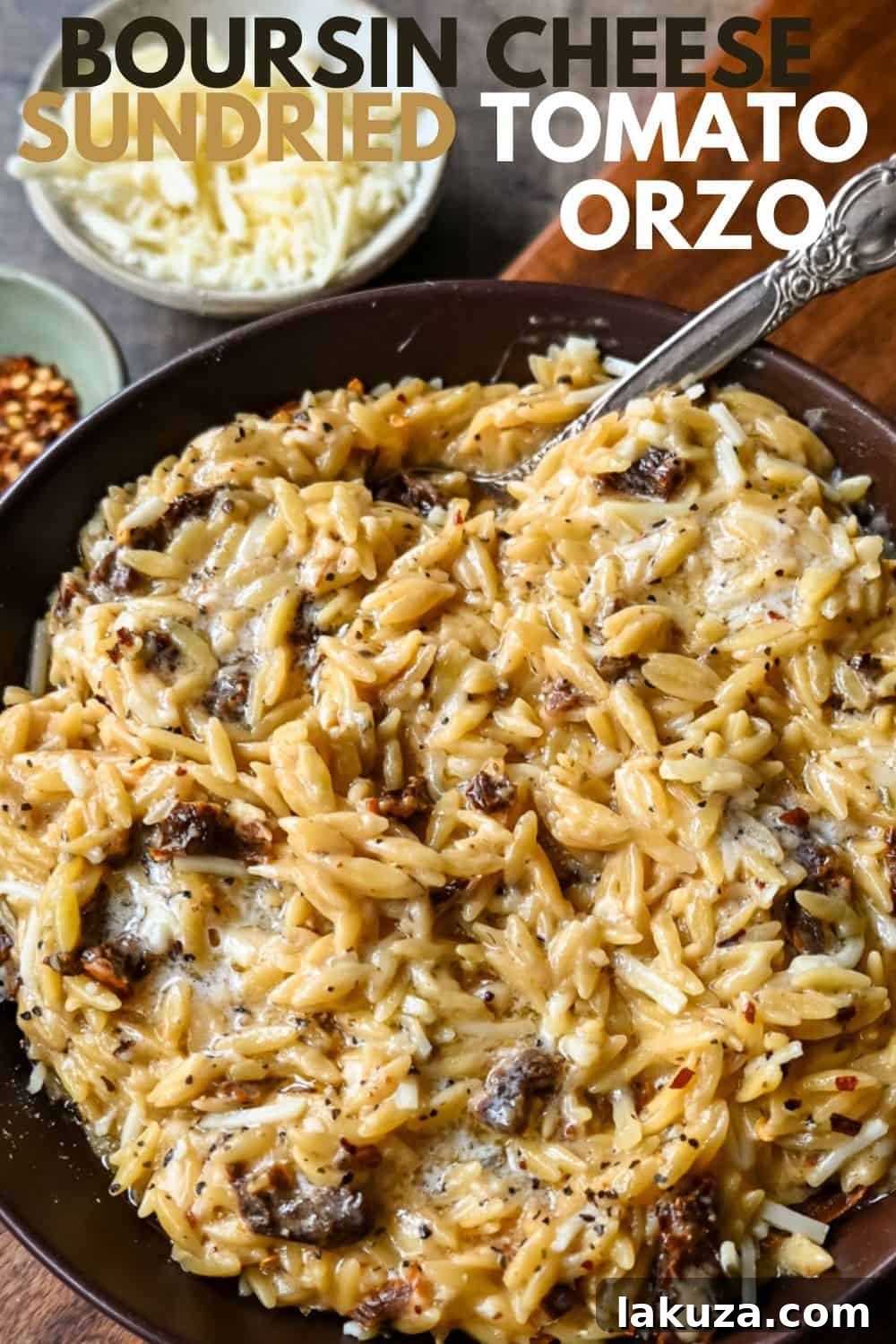 A bowl of creamy Boursin Cheese Sundried Tomato Orzo with a spoon, ready to eat. Fresh herbs garnish the top.