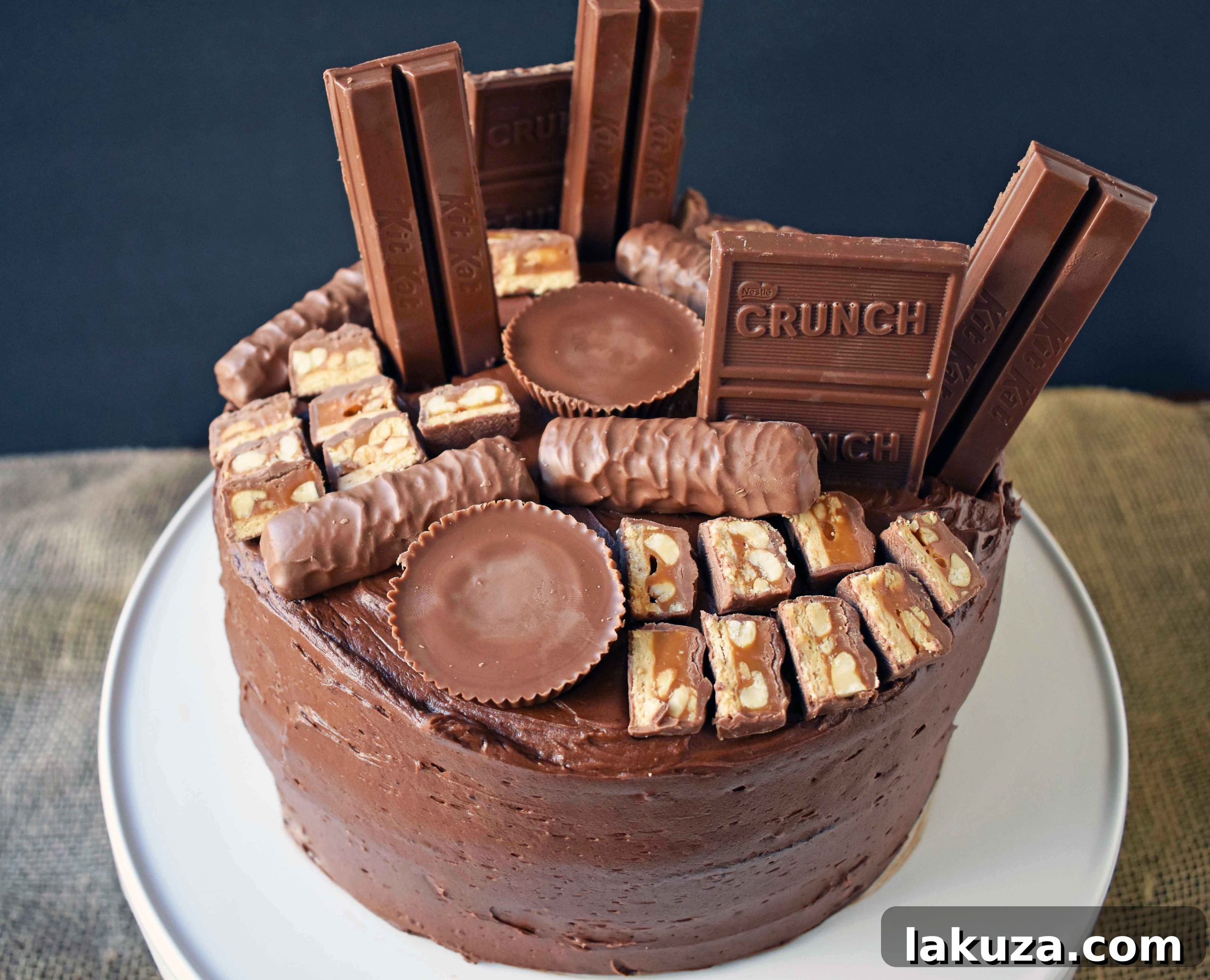A closer look at the stunning Candy Bar Stash Chocolate Cake from Modern Honey. This ultimate dessert showcases layers of rich chocolate cake, smooth chocolate buttercream, and a vibrant medley of popular candy bars like Kit Kat, Snickers, and Reese's, creating a visually appealing and utterly delicious treat.