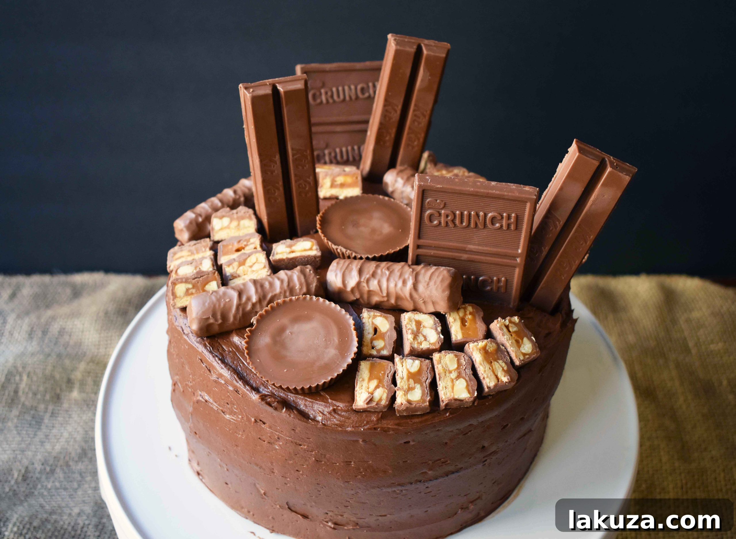 A vibrant close-up of the Candy Bar Stash Chocolate Cake by Modern Honey, showcasing its rich, dark chocolate cake base, generous swirls of smooth chocolate buttercream, and a playful arrangement of beloved candy bars. This image highlights the cake's enticing textures and decadent appeal.