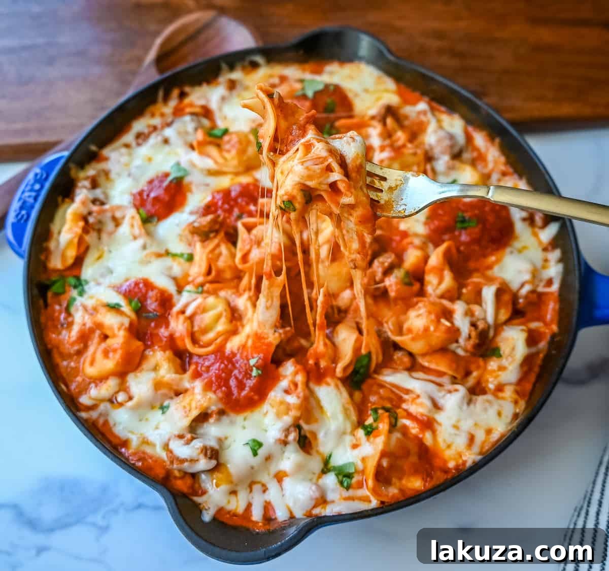 Pillowy Tortellini with Robust Sausage Ragu 4 Hands sprinkling shredded mozzarella cheese over a skillet of cheese tortellini and sausage ragu, ready for baking.