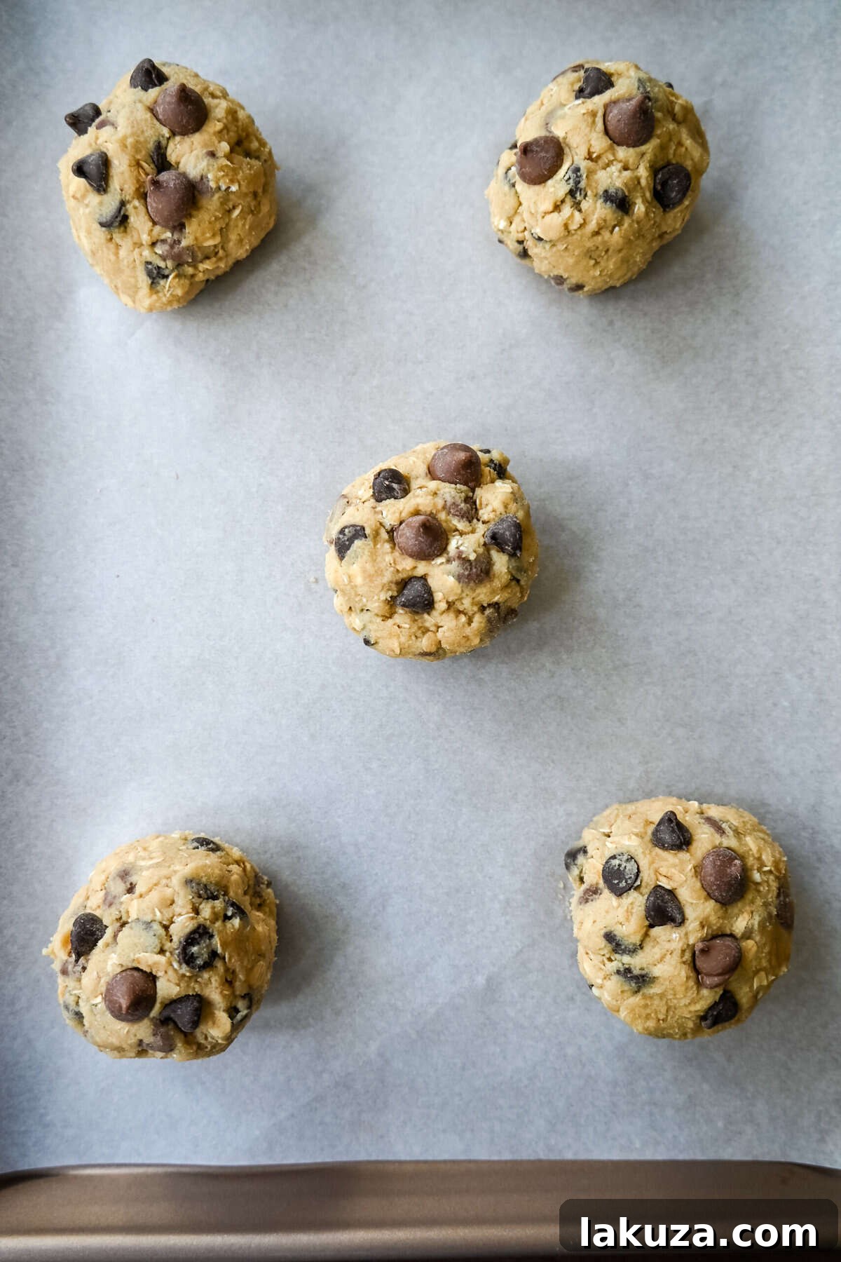 Signature Bakery Oatmeal Chocolate Chip Cookies 5 Cookie dough balls with chocolate chips ready for baking on a parchment-lined baking sheet.