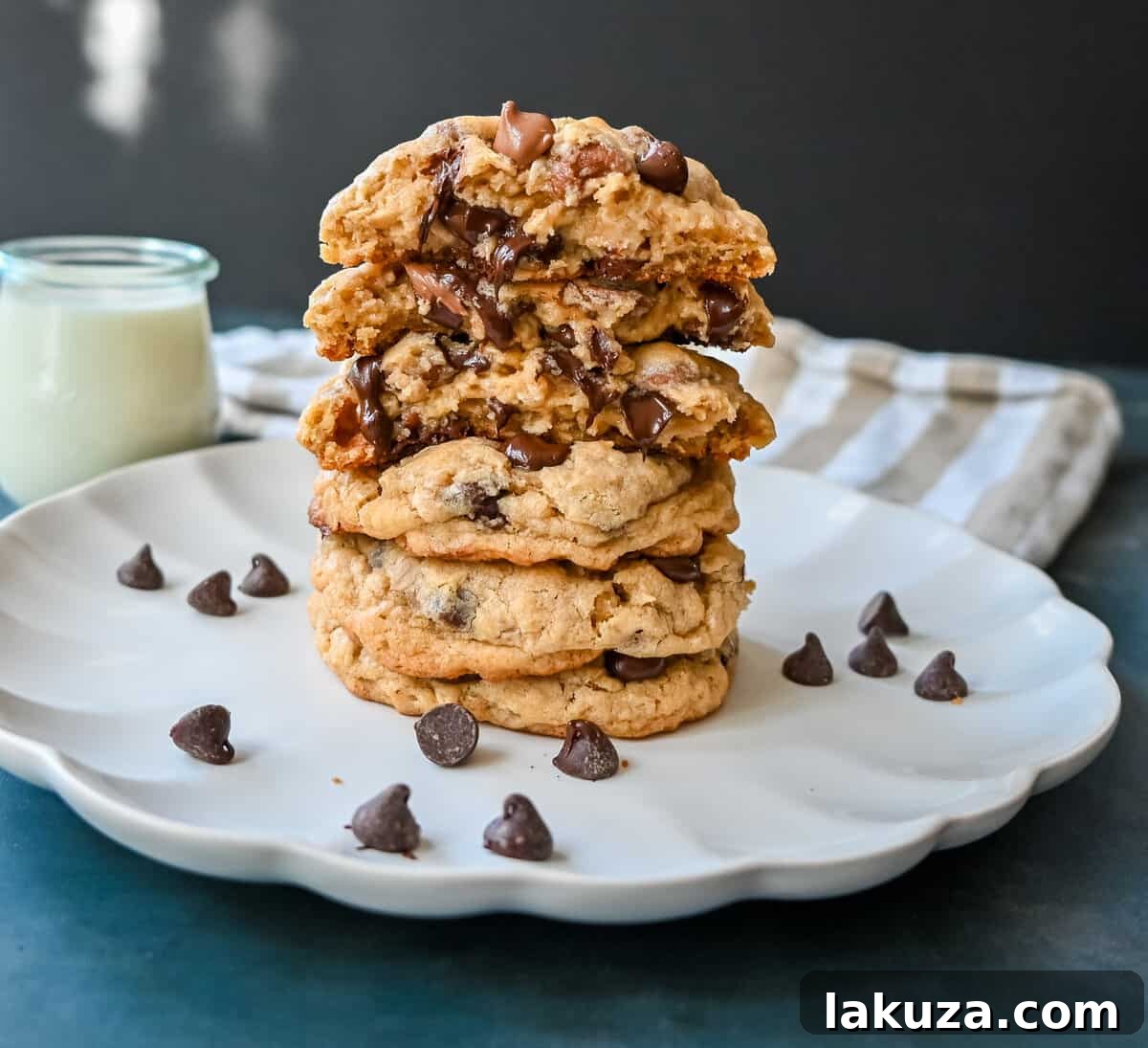 Signature Bakery Oatmeal Chocolate Chip Cookies 8 A hand reaching for a bakery-style oatmeal chocolate chip cookie on a plate.