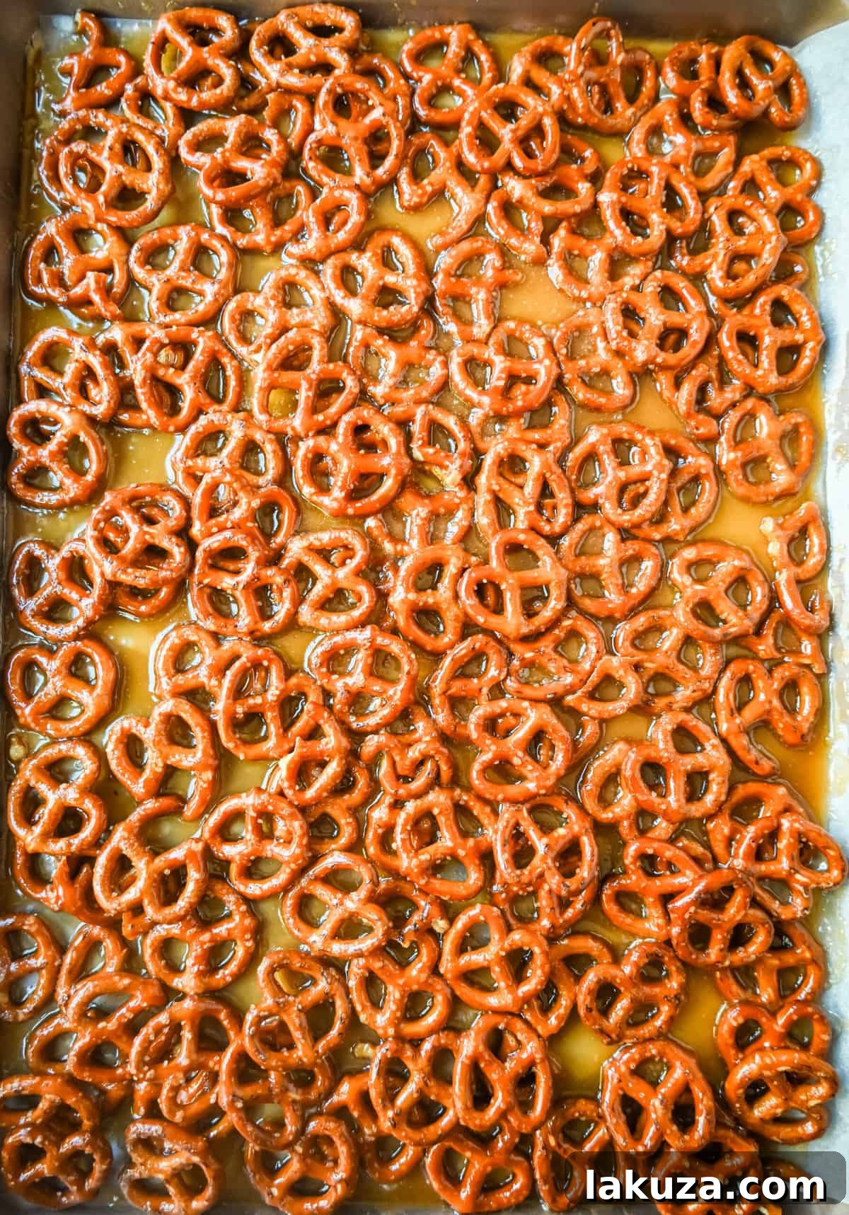 Pouring golden brown toffee mixture over a bed of mini pretzels on a baking sheet for Christmas Crack.