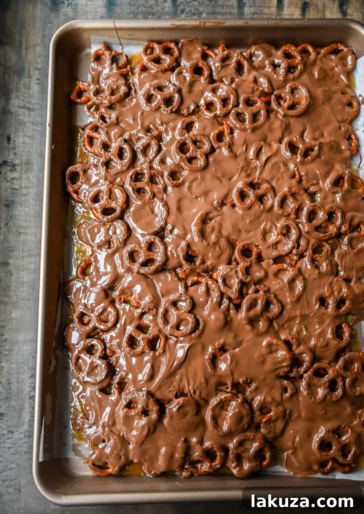 Spreading melted chocolate over the hot toffee and pretzel layer for homemade Christmas Crack.