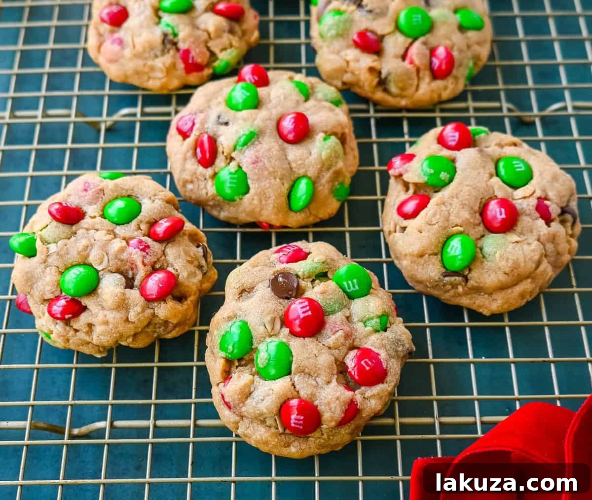 A batch of freshly baked Christmas Monster Cookies arranged on a cooling rack, showcasing their vibrant red and green M&M's and irresistible chewy texture, with holiday decorations in the background.