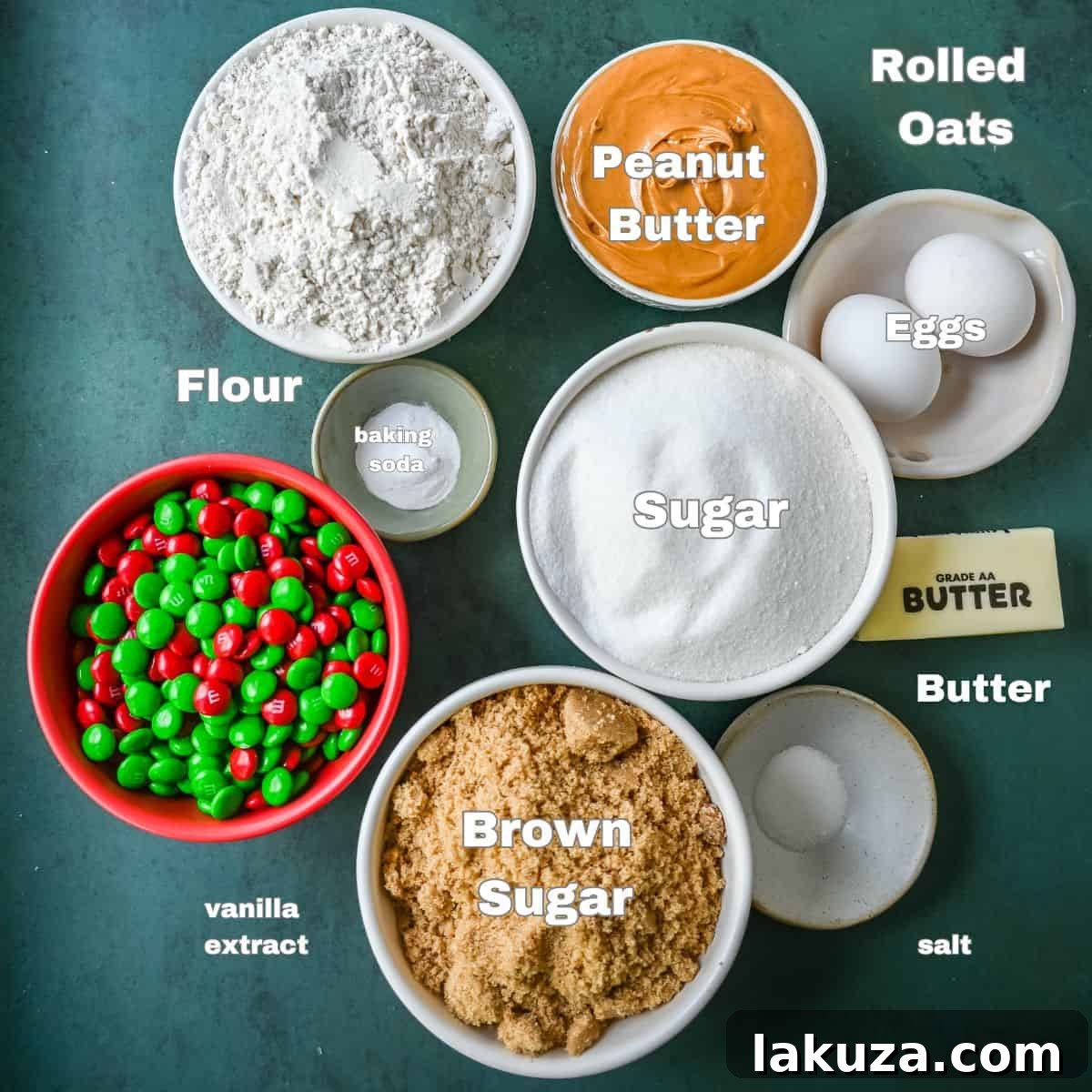 A visual display of all the ingredients needed for Christmas Monster Cookies, including softened butter, brown sugar, granulated sugar, creamy peanut butter, large eggs, vanilla extract, rolled oats, all-purpose flour, baking soda, salt, chocolate chips, and festive red and green M&M's, arranged on a rustic wooden surface.