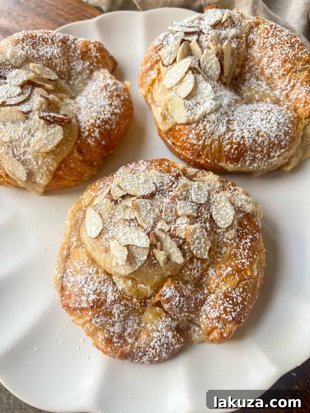 Close-up of a freshly baked almond croissant, showcasing its flaky texture and a generous sprinkle of sliced almonds on top.