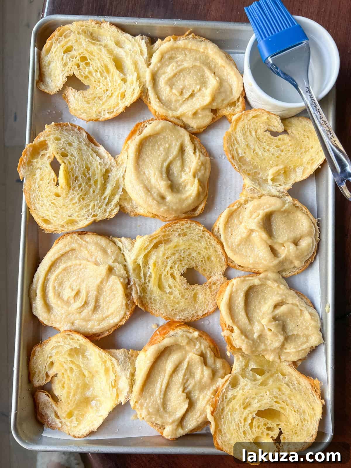 A croissant being filled with creamy almond frangipane, ready for the top half and sliced almonds.