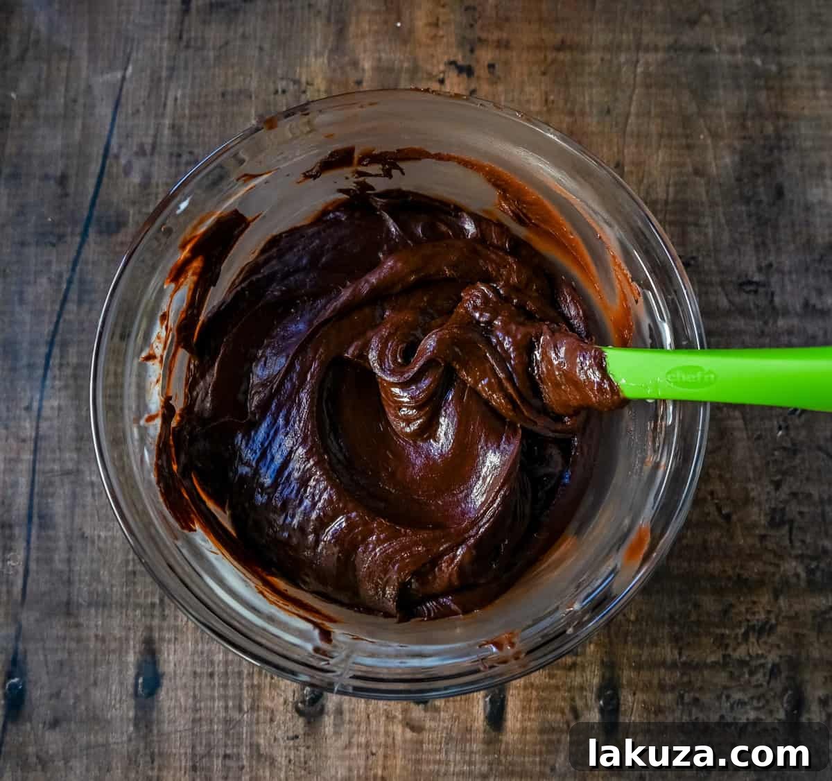 The melted mixture of chocolate and sweetened condensed milk is being stirred in a microwave-safe bowl until perfectly smooth and glossy.