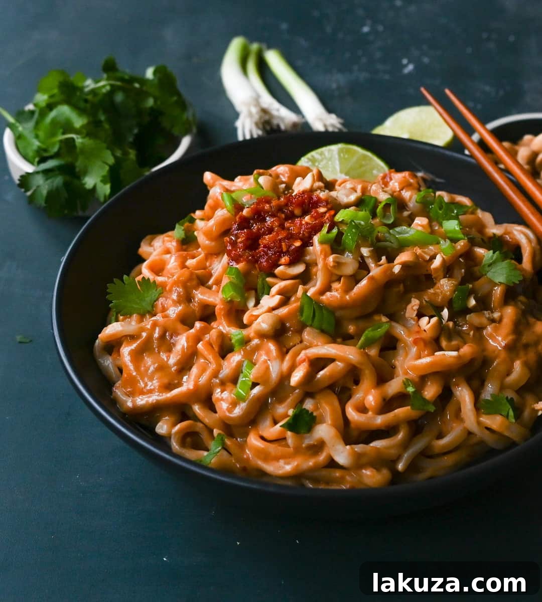 Creamy Chili Peanut Noodles 5 A generous serving of Spicy Peanut Noodles in a bowl, with a focus on the saucy texture and scattered garnishes. It highlights the quick preparation time of under 15 minutes.