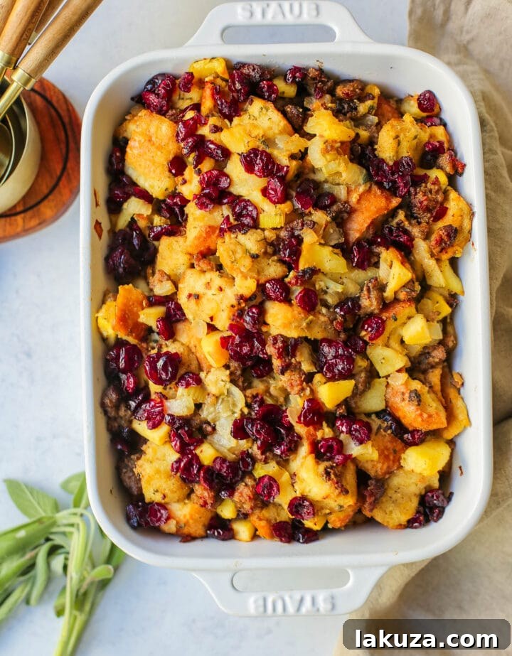 Ingredients for Classic Sausage Herb Stuffing laid out on a wooden board, including bread, sausage, apples, cranberries, and herbs.