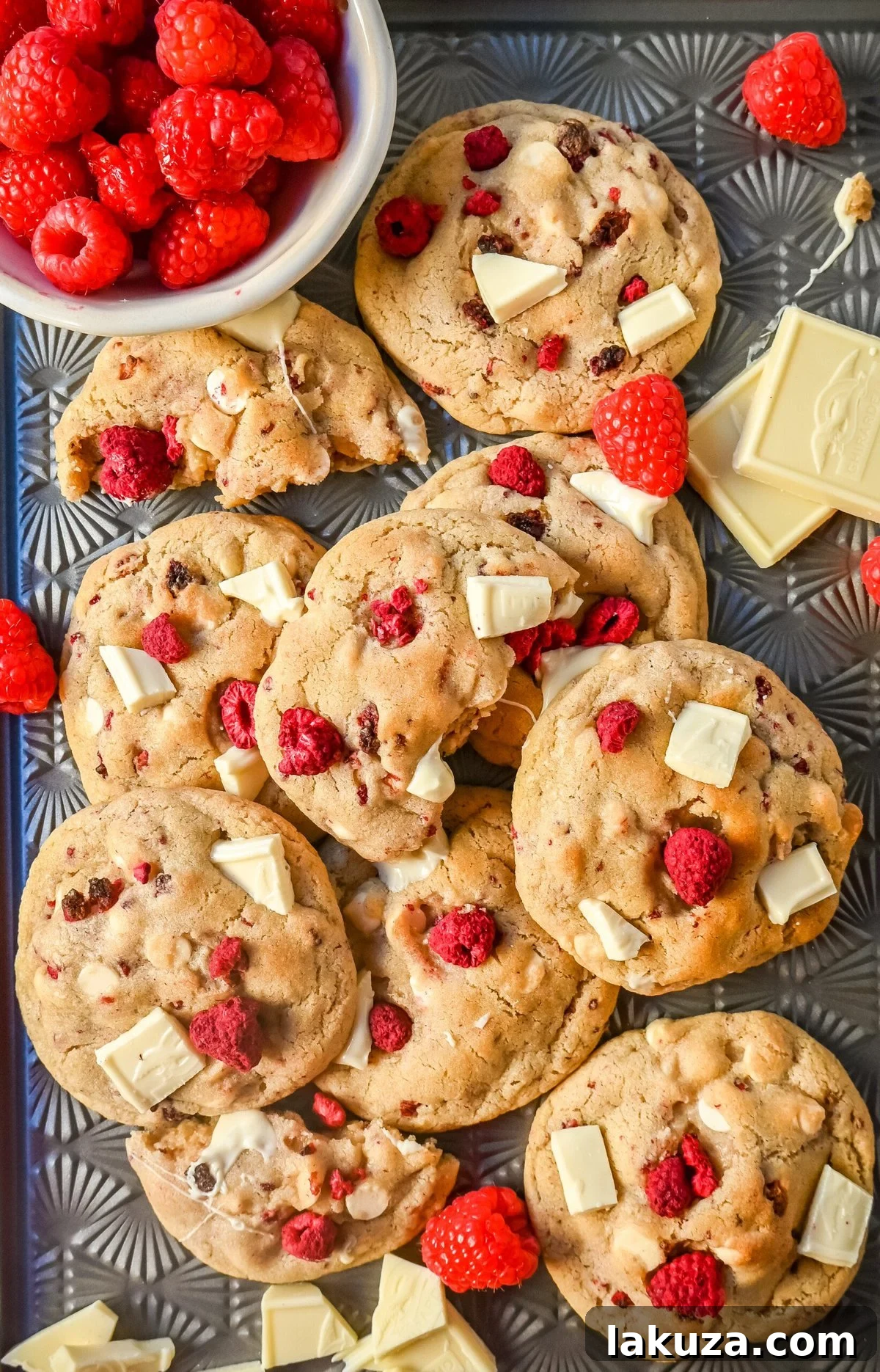 Ingredients for white chocolate raspberry cookies laid out: freeze-dried raspberries, white chocolate chunks, butter, eggs, flour, and sugars.
