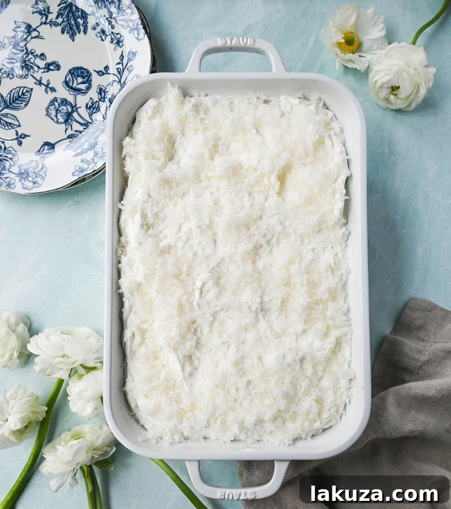 Close-up of a slice of Coconut Poke Cake, showing the moist interior soaked with milk and topped with cream.