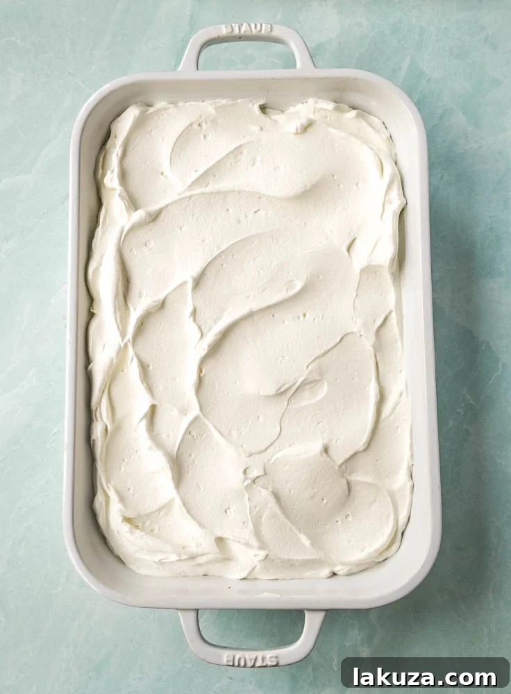 A freshly made Coconut Poke Sheet Cake, topped with generous whipped cream and toasted coconut, ready to be served.