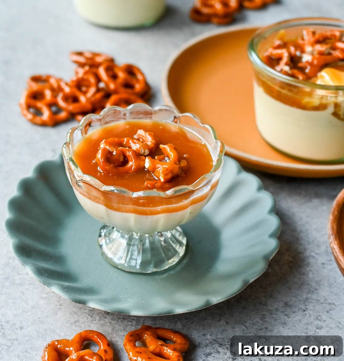 Close-up shot of individual servings of vanilla panna cotta, topped with golden salted caramel and broken pieces of toffee pretzels, showcasing the layers and textures.