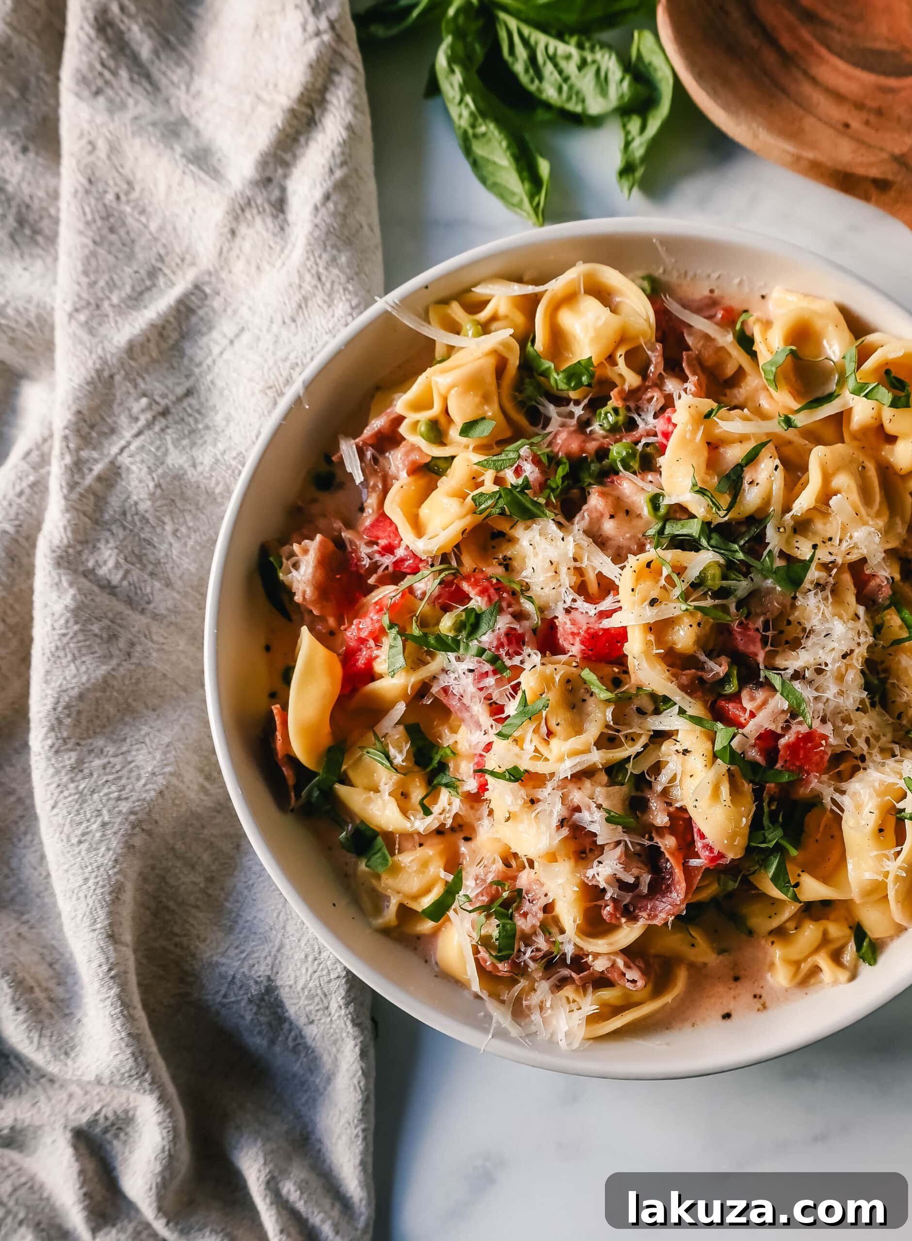 A close-up of creamy tortellini with crispy prosciutto and vibrant green peas, ready to be served.