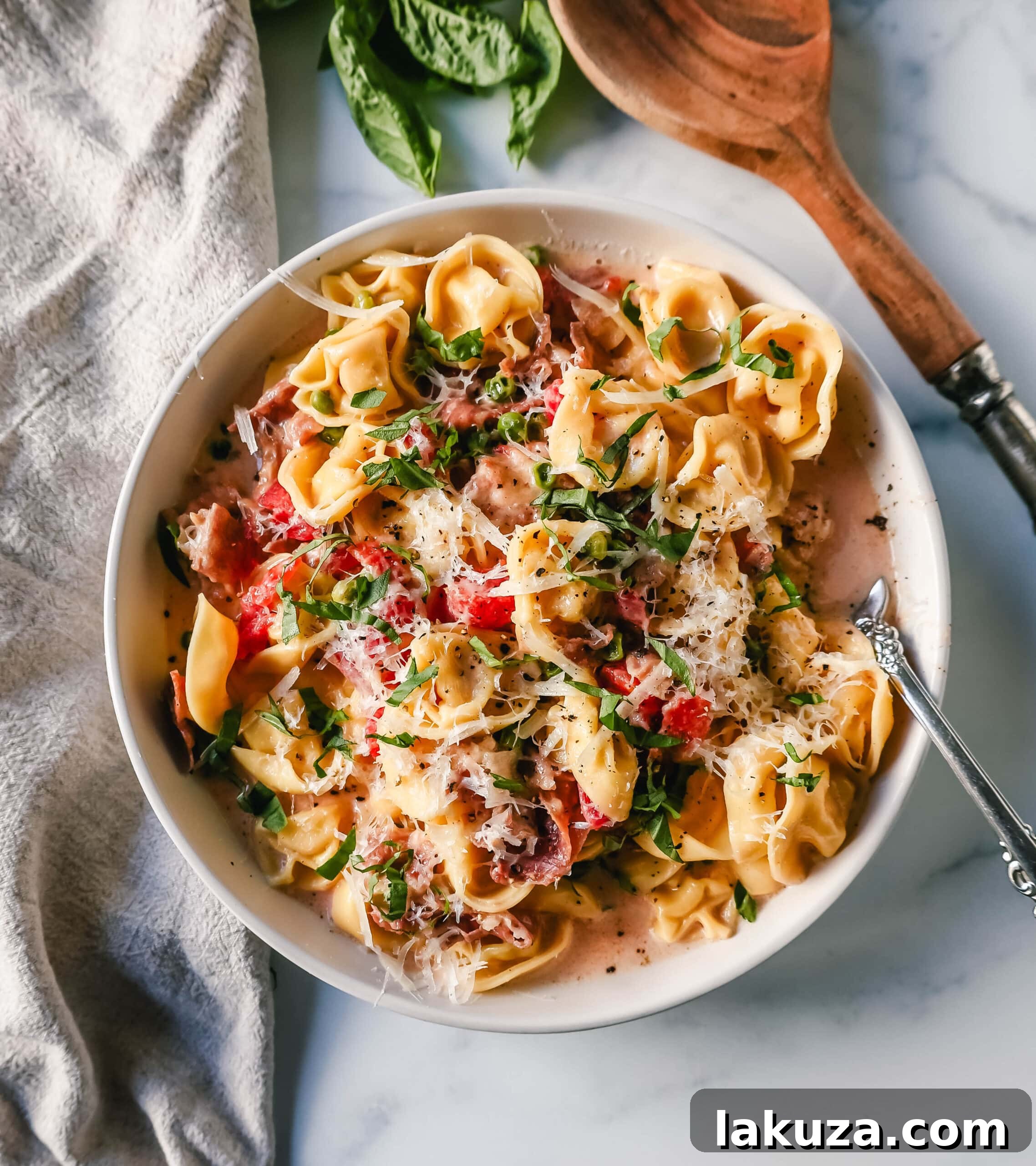 Ingredients for Creamy Tortellini with Prosciutto and Peas laid out on a table, including tortellini, prosciutto, tomatoes, cream, and cheese.