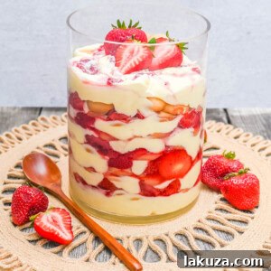 A beautifully presented serving of Magnolia Bakery Strawberry Shortcake Pudding in a glass, topped with a dollop of whipped cream and a slice of fresh strawberry.