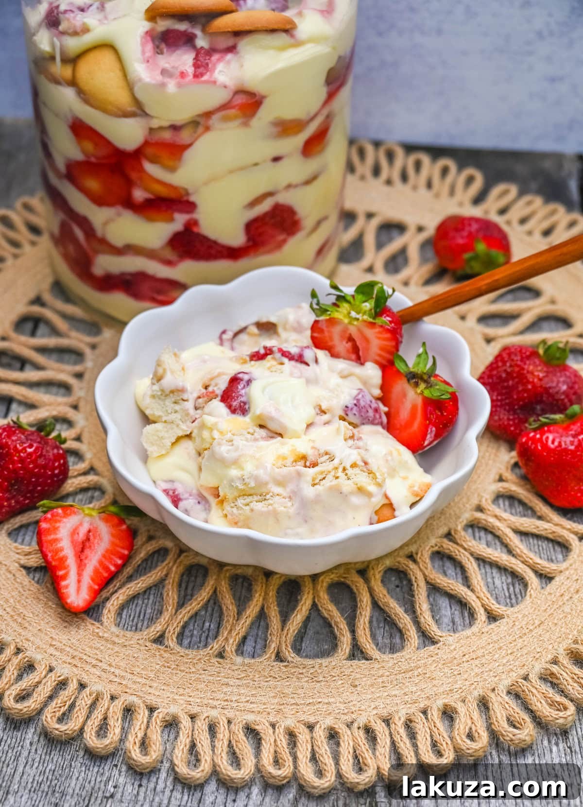Layers of Nilla wafers, fresh strawberries, and creamy vanilla pudding visible through the glass of a trifle bowl.