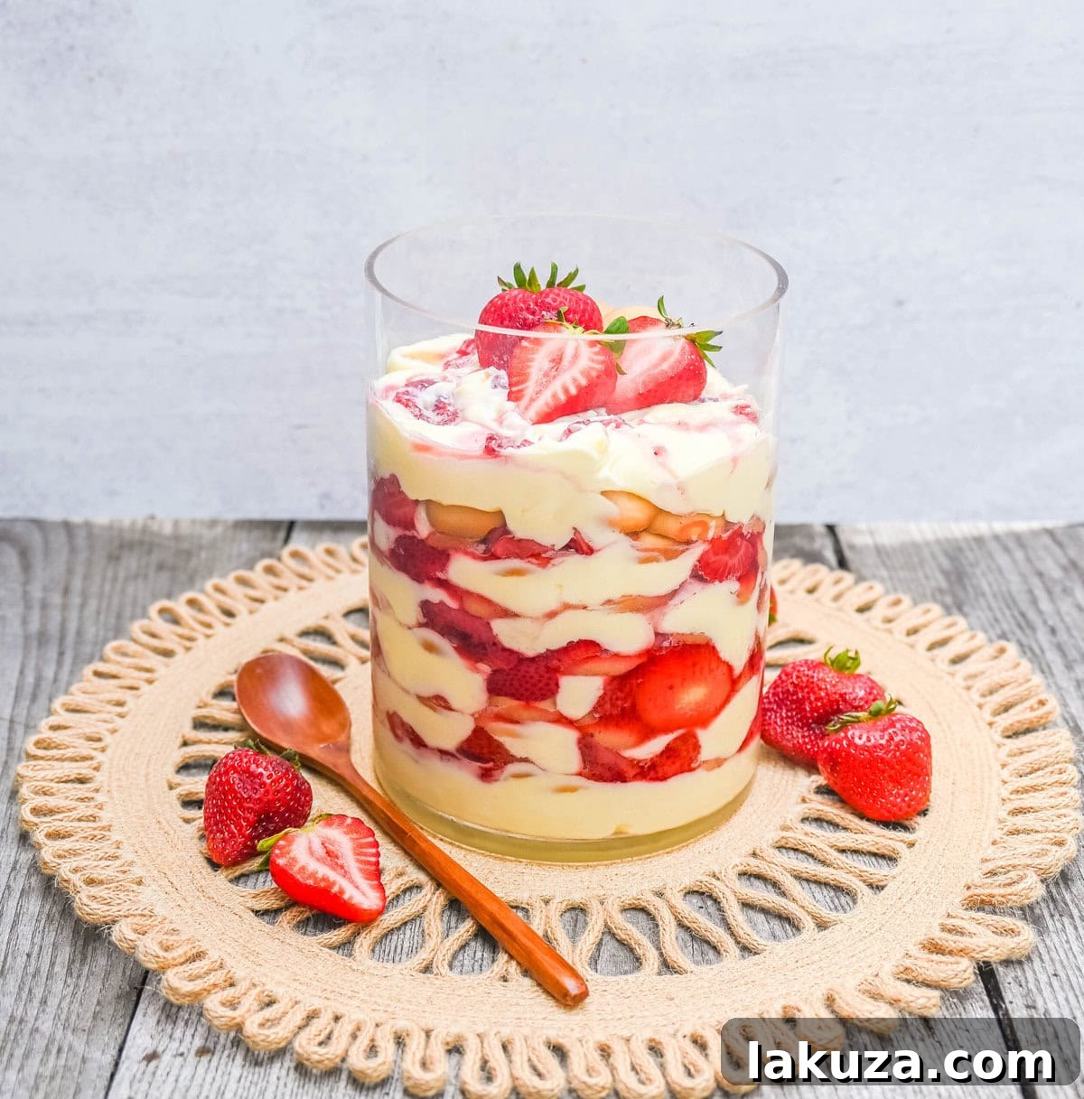 A serving spoon scoops into a glass of Magnolia Bakery Strawberry Shortcake Pudding, showing its creamy layers and a softened Nilla wafer.